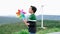 Progressive young asian boy playing with wind turbine toy at wind turbine farm.