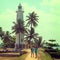 The promenade and the lighthouse, green palm trees and tourists