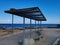 A promenade made of stone tiles with a wooden bench and a sunshade along the rocky coast of the Mediterranean Sea