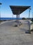 A promenade made of stone tiles with a wooden bench and a sunshade along the rocky coast of the Mediterranean Sea