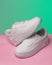 Promotional photo of pair of new white women's or teen sneakers on colored background.