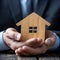 Property safeguarded Businessman protects wooden home model with his hand