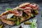 Prosciutto sandwich, Ciabatta with prosciutto, sun-dried tomatoes, gherkins, parmesan and arugula, Food recipe background. Close