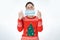 Protection from coronavirus. A young woman with a stupid expression in her eyes, wearing a Christmas sweater, holds a medical mask