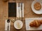 Protective facial mask with cookies, croissant, cutlery and a cup of coffee on a wooden table in the cafe.