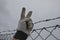 Protesting man in gray tactical gloves overcome a barbed wire fence and get behind a wire fence. showing fingers on hand a sign of