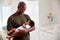 Proud Father Cuddling Baby Son In Nursery At Home