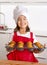 Proud female child presenting her self made muffin cakes learning baking wearing red apron and cook hat smiling happy