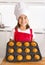 Proud female child presenting her self made muffin cakes learning baking wearing red apron and cook hat smiling happy
