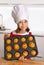 Proud female child presenting her self made muffin cakes learning baking wearing red apron and cook hat smiling happy