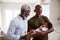 Proud Grandfather With Adult Son Cuddling Baby Grandson In Nursery At Home