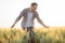 Proud happy young farmer walking through wheat field, gently touching plants with his hands