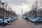 Provincial Holland. Cityscape With Solar Eclipse, Street Of Small Flanders Town With Gothic Church, Two Rows Of Cars And SIngle B