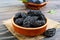 Prunes in a clay bowl and fresh plums, leaves on a wooden table.