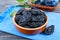 Prunes in a clay bowl and fresh plums, leaves on a wooden table