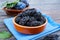 Prunes in a clay bowl and fresh plums, leaves on a wooden table.