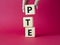 PTE - Pearson Tests of English symbol. Wooden cubes with word PTE. Businessman hand. Beautiful red background. Business and PTE