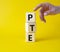 PTE - Pearson Tests of English symbol. Wooden cubes with word PTE. Businessman hand. Beautiful yellow background. Business and PTE