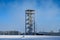 Public wood and steel observation tower in winter with a snowman in a field