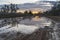 Puddle on a path in the field in which the sunset is reflected.