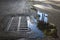 Puddle on the pavement, palm trees reflected in the water. water flows into the sewer drain