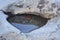 Puddle in a rock with pebbles and a leaf submerged