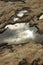 Puddle of water reflecting sunshine on rocks stones on brown color