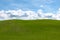 Puffy white clouds and blue sky over a huge beautiful idyllic vibrant green grassy field with gently rolling hills in the backgrou