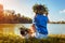 Pug dog and its master chilling by river wearing flower wreaths. Happy puppy and woman enjoying summer nature outdoors