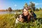 Pug dog and its master chilling by summer river wearing flower wreaths. Happy puppy licking woman