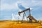 Pump jack oil gas well on red soil with storage tanks on horizon under dramatic sky