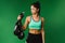 A pumped-up brunette girl seriously looks at the boxing gloves held in her hand on a green background with side space.
