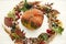 Pumpkin in autumn wreath of fall leaves, red berries, acorns, anise, nuts, autumn flowers on white wood. Happy Thanksgiving. Cozy