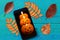 Pumpkin candle picture on a mobile phone with colorful autumn leaves captured from above top view, flat lay.