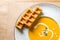 Pumpkin and carrot soup with cream and Belgian waffles on rustic wooden background. Flat lay with empty space