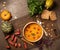 Pumpkin cream soup, served with smoked mini sausage and bread, parsley, basil, seeds on a cutter board. Stone background