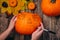 Pumpkin decoration. Halloween decoration concept. Close up hands with pumpkin on wooden vintage table. Draw make a draft