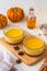 Pumpkin flan, a cold baked dessert of pumpkin puree, eggs, cream and sugar in glass ramekins on a wooden board on a light concrete