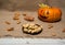 Pumpkin with a funny painted face, homemade cookies `witch`s finger`, autumn leaves on a textile background.