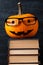 Pumpkin with painted face, glasses on a stack of books, halloween design. Concept of holiday all saints' eve, greeting card