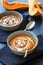 Pumpkin soup in two plates with cutted pumpkins in background, homemade summer or autumn hot soup