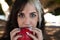 Punky girl with blonde and brunette hair holds a red apple in her hands and stares at it. The girl is a witch from the fairy tale