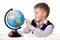 Pupil with a globe. Cheerful satisfied pupil sitting at the desk on the white background