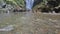 Pure crystal transparent water flowing above colorful pebbles and stones in mountain river against background waterfall