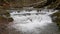 Purest mountain creek in the forest. Stream of water moves between the stones covered with moss. Small river with rocks