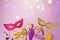 Purim holiday concept with carnival mask and party supplies on purple background with bokeh lights.