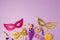 Purim holiday concept with carnival mask and party supplies on purple background. Top view from above