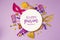 Purim holiday concept with white paper circle and party supplies on purple background.