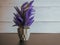 Purple artificial lavender like plant sitting in a black slate surface with a gray shiplap background.  Pretty purple home decor