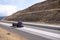 Purple big rig semi truck with flat bed semi trailer transporting covered cargo on the road between the hills in Oregon